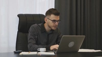Man sitting by his desk, working on his laptop.