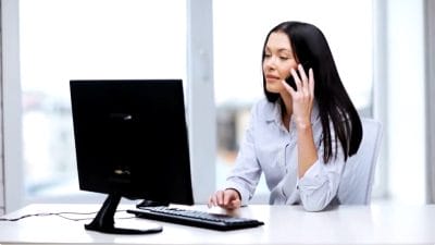 Woman speaking on phone while working at computer desk.